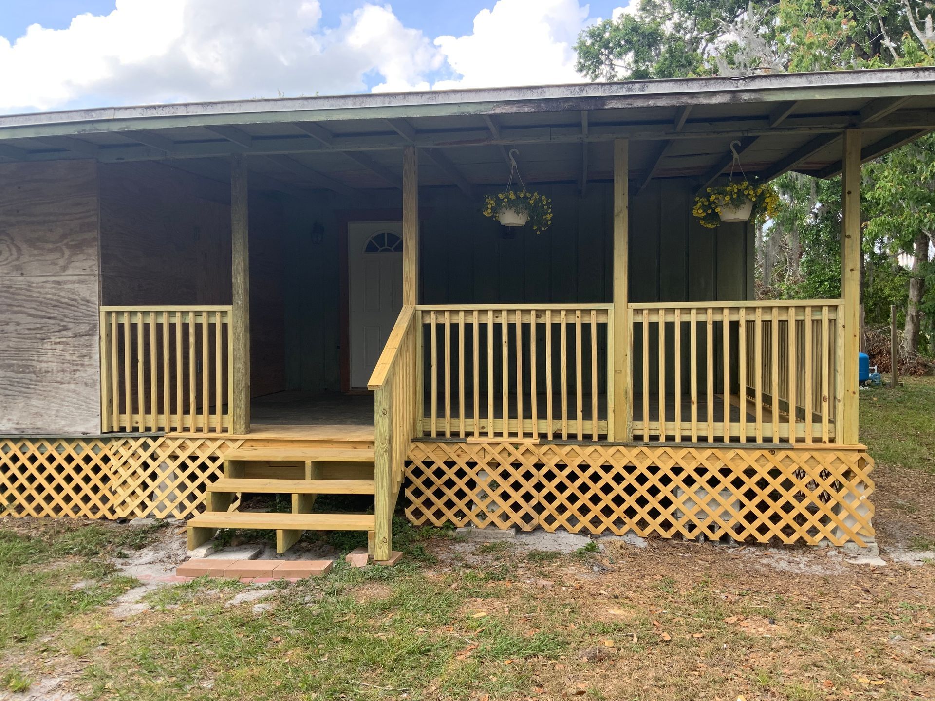 Wooden porch with latticework and railing; hanging flower baskets, door visible.
