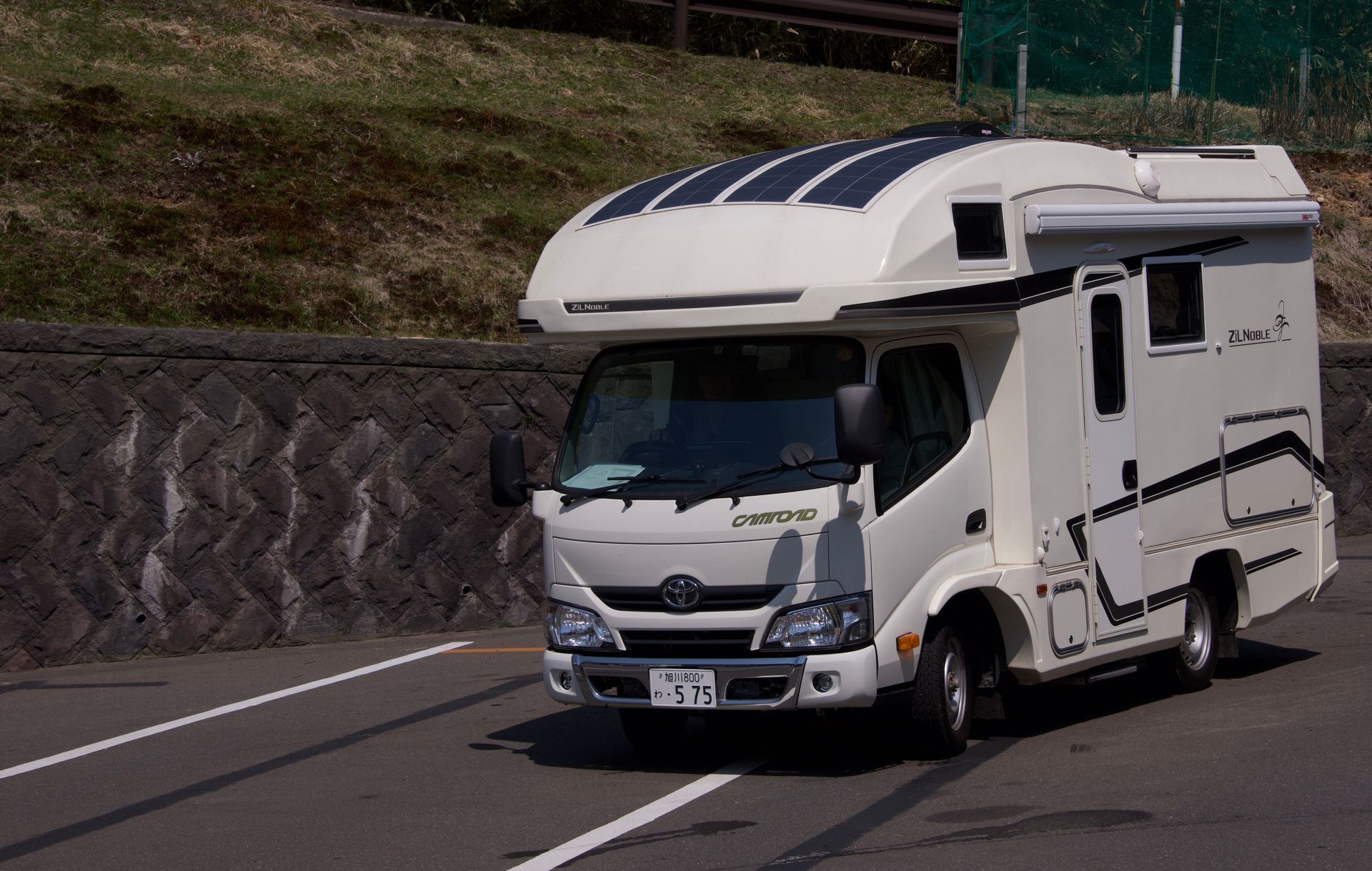 White motorhome driving on a highway curve beside a rocky embankment.