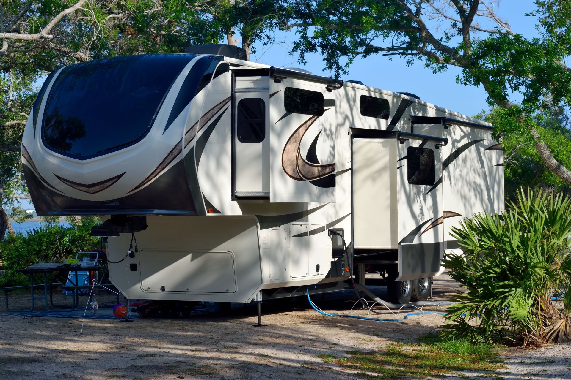 Large white and black fifth-wheel RV parked under trees at a campsite