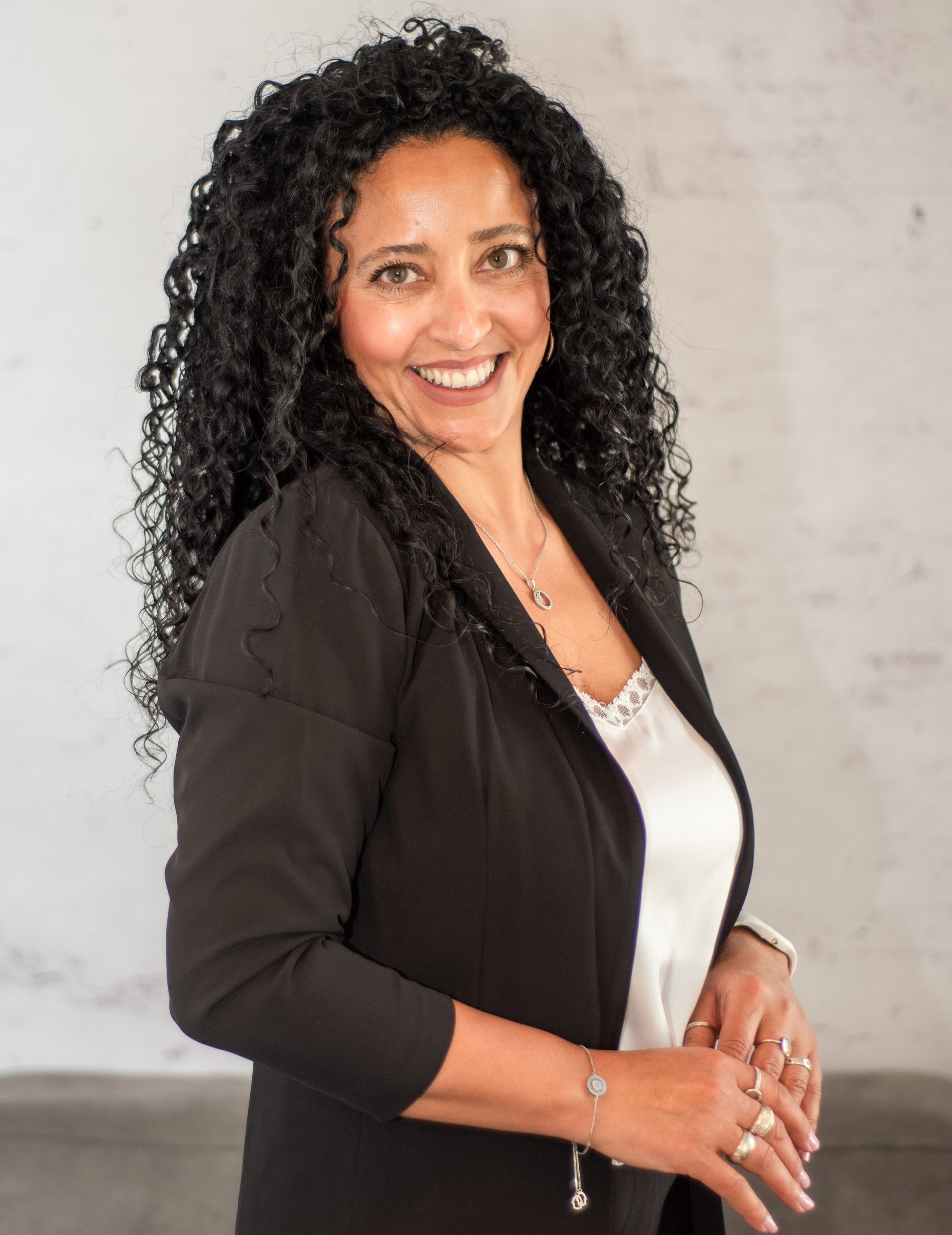 אישה עם שיער מתולתל לובשת ז'קט שחור וחולצה לבנה.