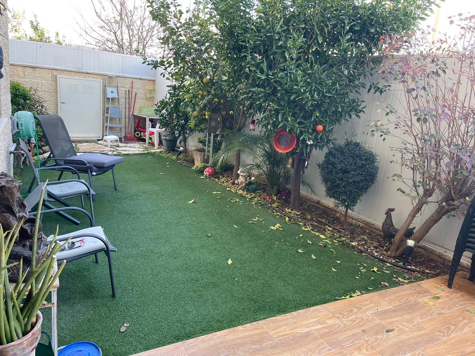 חצר אחורית עם מדשאה, כיסאות, שולחן ועץ.