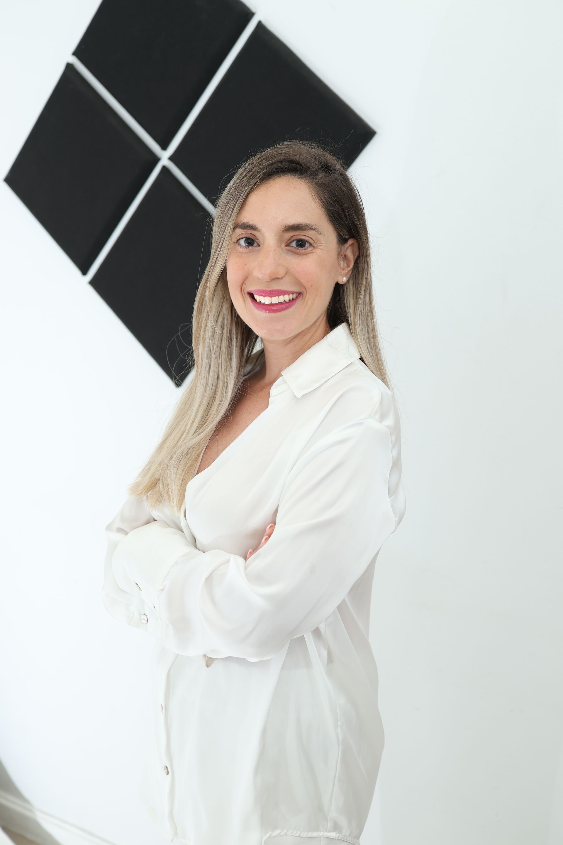 אישה בחולצה לבנה מצטלמת בזרועותיה שלובות.