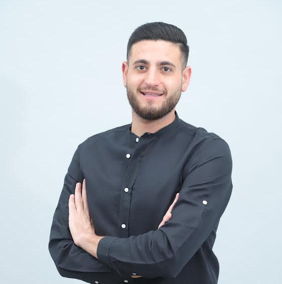 גבר עם זקן לובש חולצה שחורה עם זרועות שלובות.