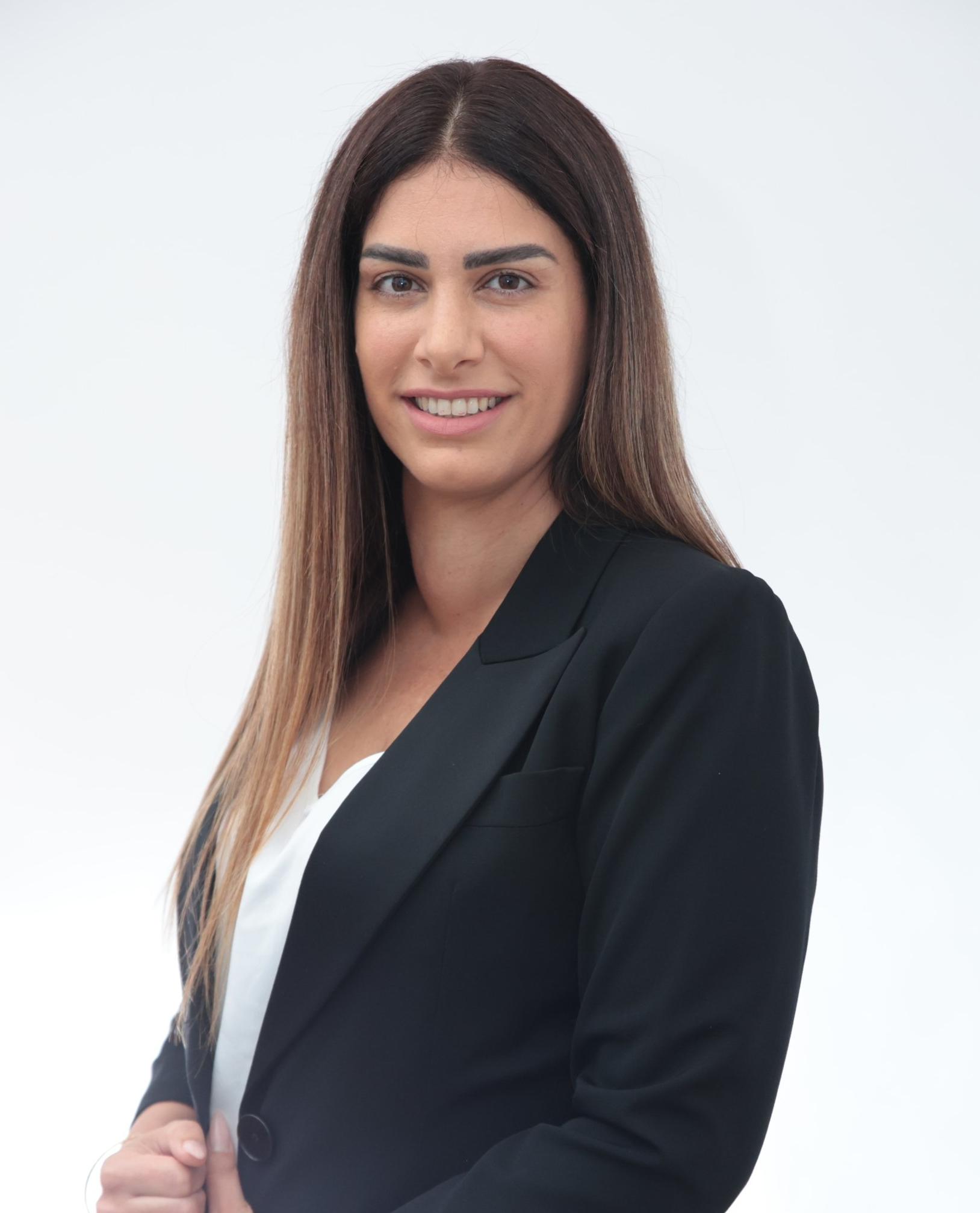 אישה עם ז'קט שחור וחולצה לבנה מחייכת למצלמה.