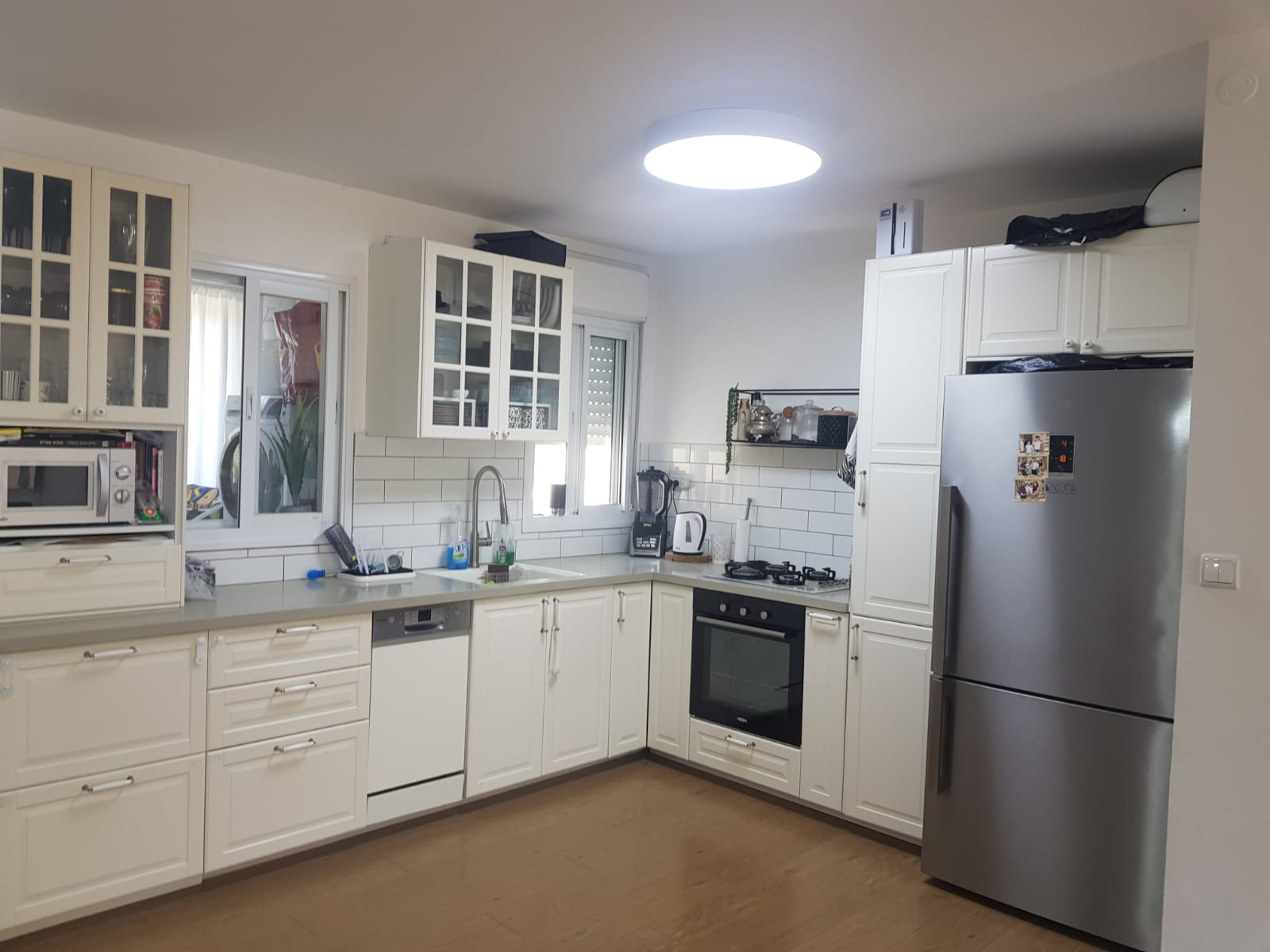 מטבח עם ארונות לבנים ומקרר נירוסטה.