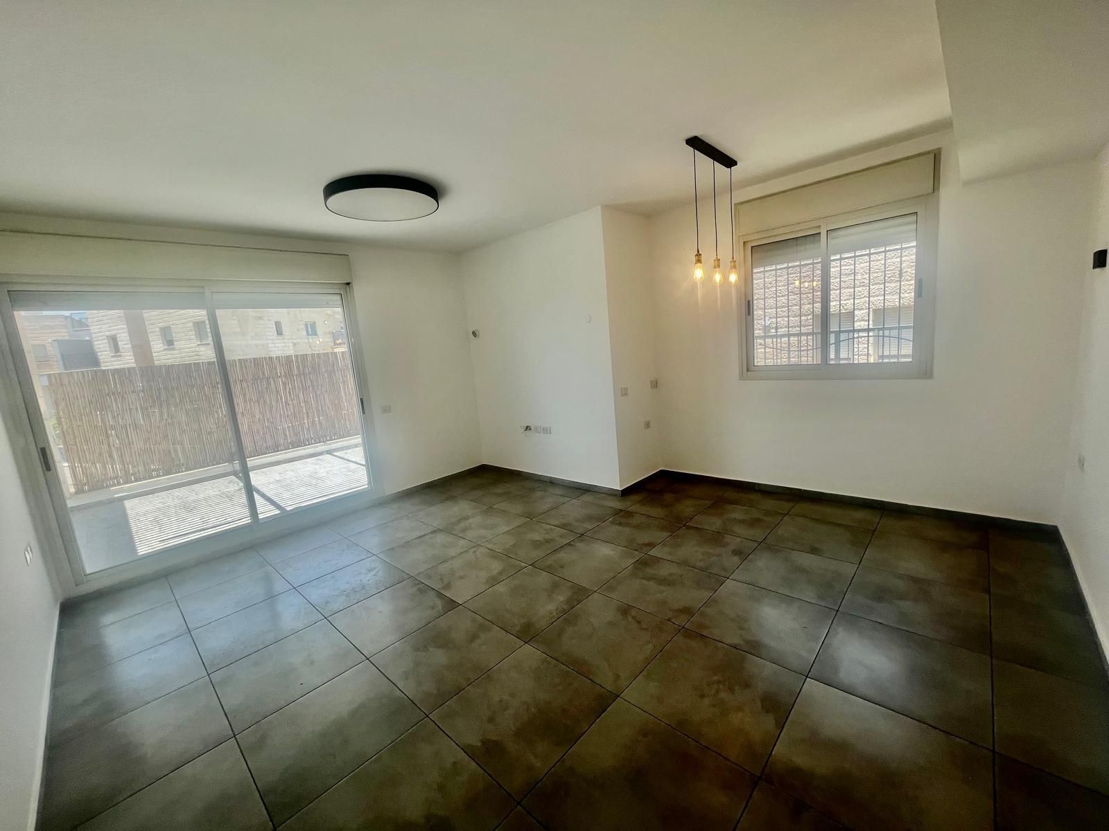 סלון ריק עם דלתות הזזה מזכוכית ואור תקרה.