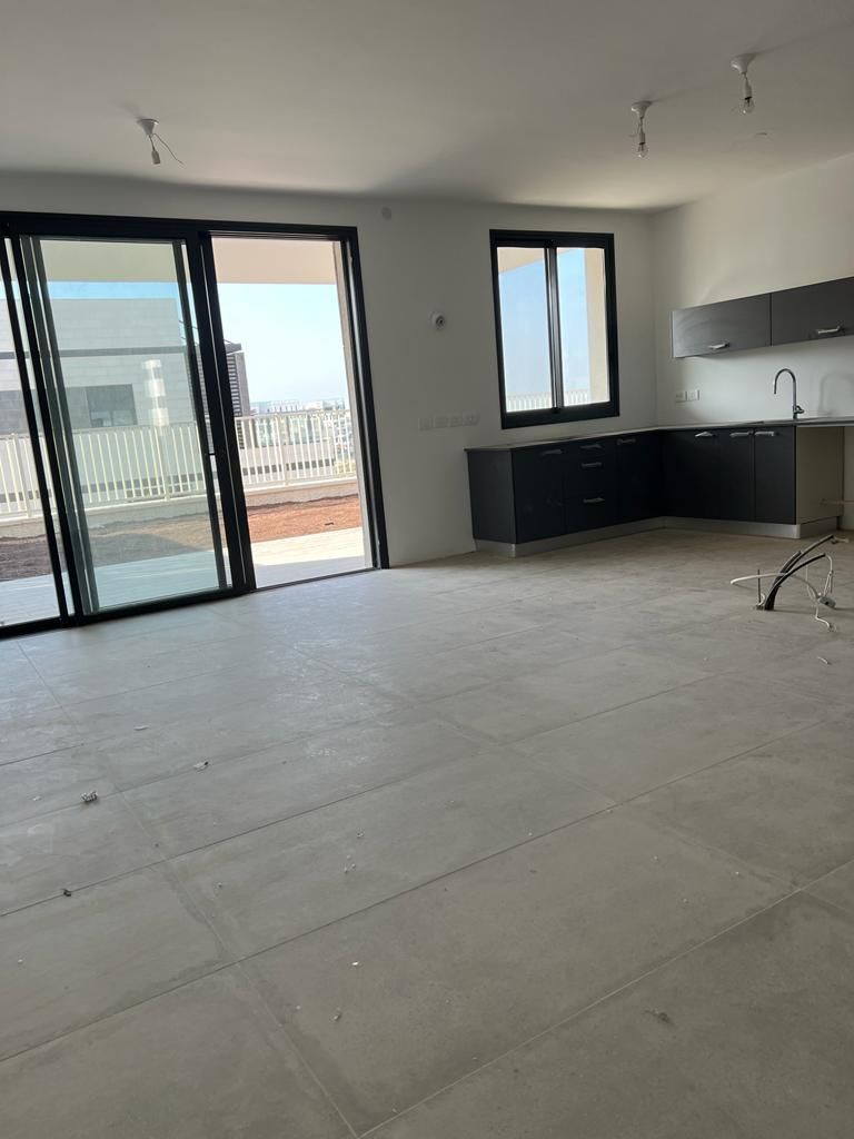 חדר ריק גדול עם מטבח ודלתות הזזה מזכוכית.