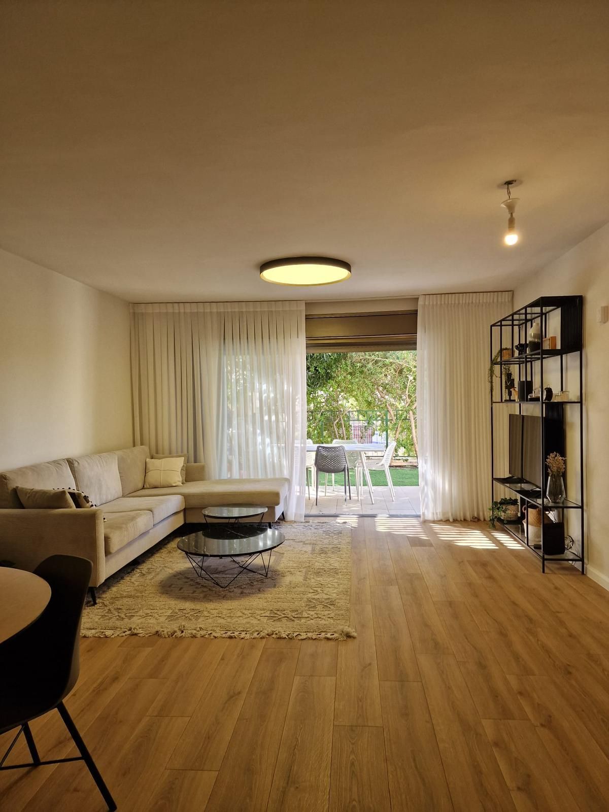 סלון עם ספה, שולחן, כיסאות ודלתות הזזה מזכוכית.