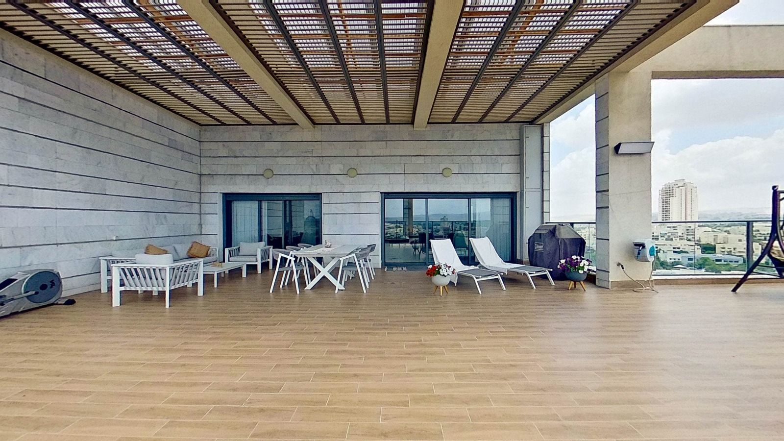 מרפסת גג גדולה עם פרגולה, כיסאות, שולחנות ונדנדה.