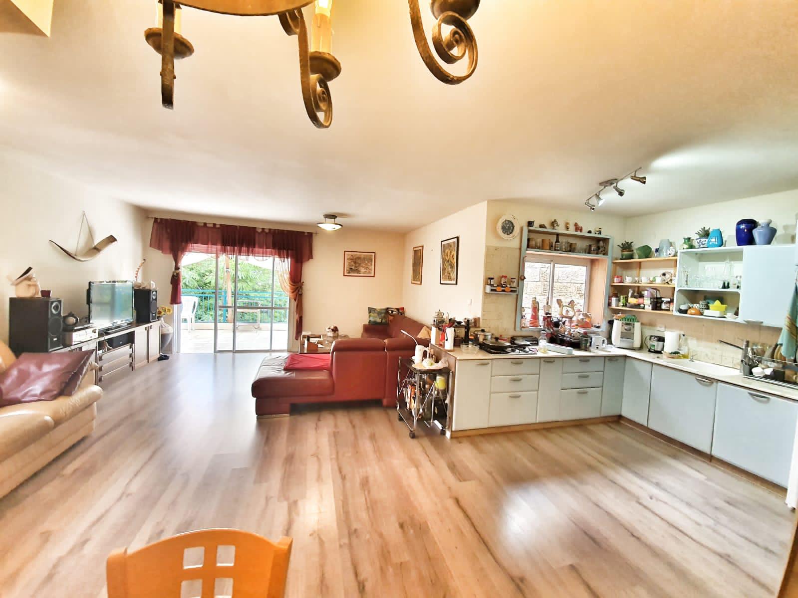 סלון עם ספה ומטבח עם נברשת תלויה מהתקרה.