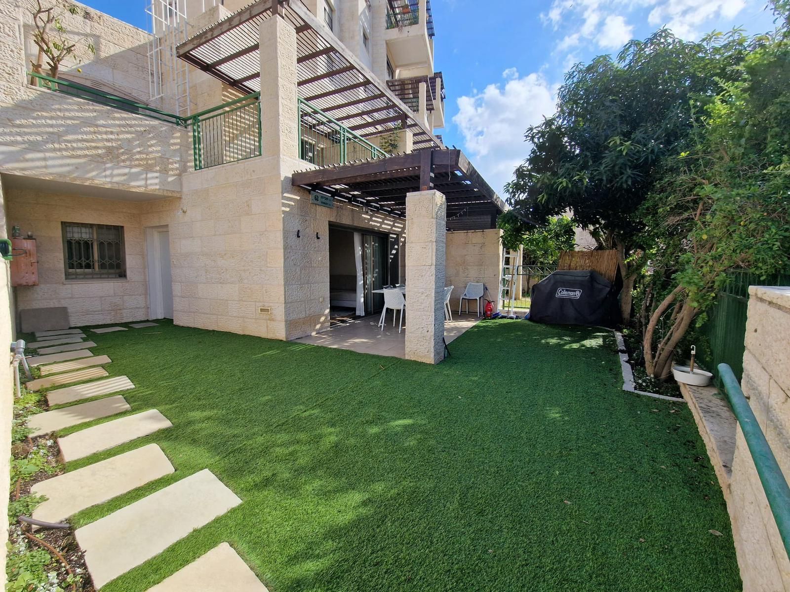 יש מדשאה גדולה מול בית עם פרגולה.