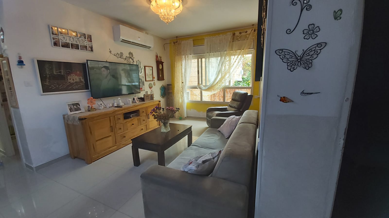 סלון עם ספה, שולחן, טלוויזיה ומדבקות פרפר על הקיר.