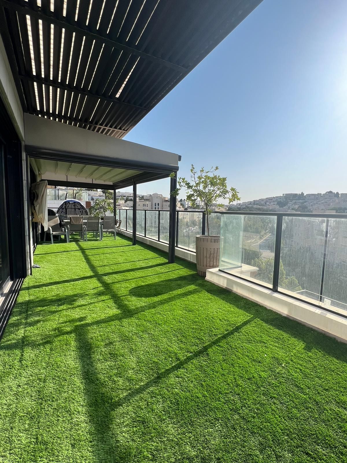 מרפסת עם מדשאה ירוקה ופרגולה.