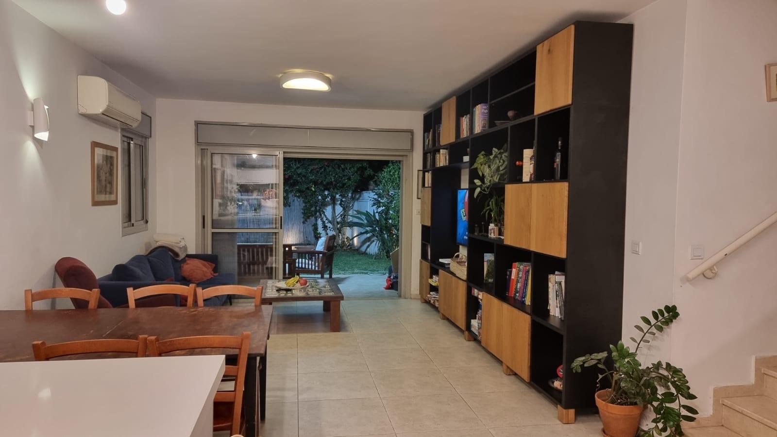 סלון עם שולחן וכיסאות ומדף ספרים.