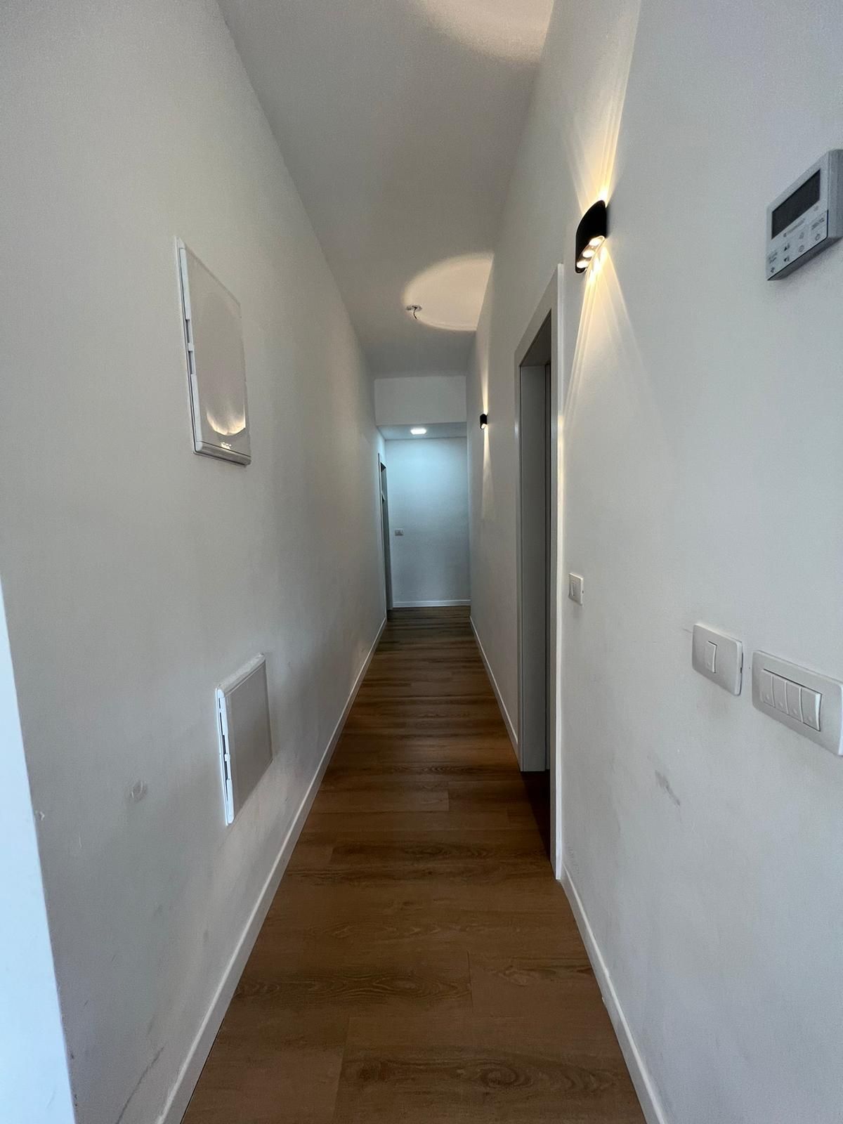 מסדרון ארוך עם קירות לבנים ורצפות עץ המובילים לדלת.