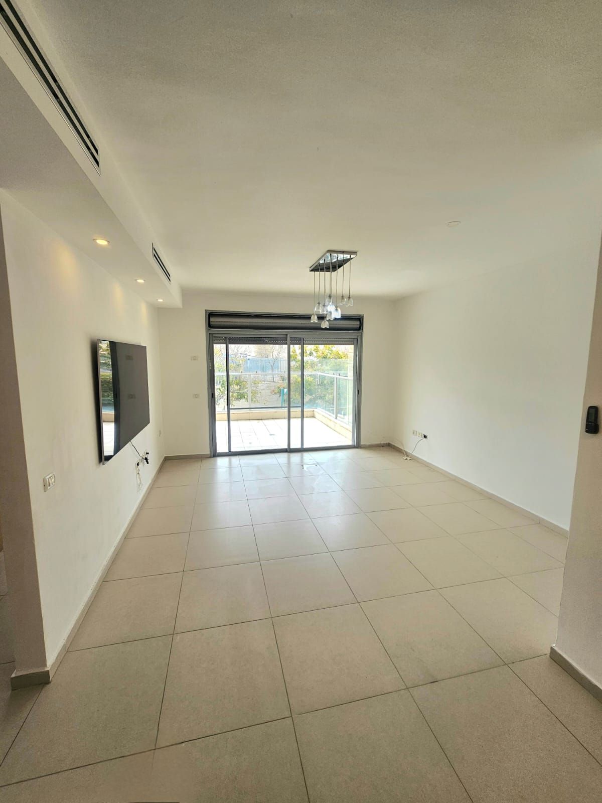 סלון ריק עם דלת הזזה מזכוכית וטלוויזיה בעלת מסך שטוח.