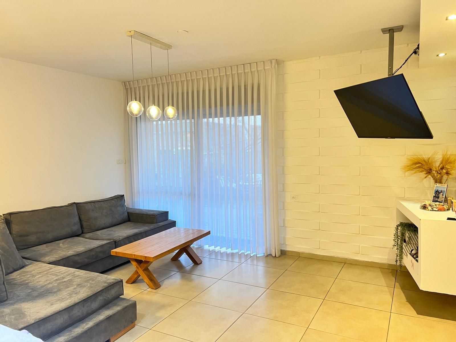 סלון עם ספה, שולחן קפה, טלוויזיה ודלתות הזזה מזכוכית.