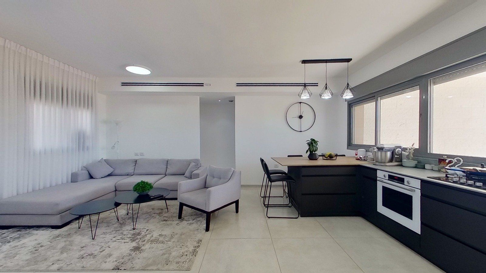 סלון עם ספה וכיסאות ומטבח עם שעון על הקיר.