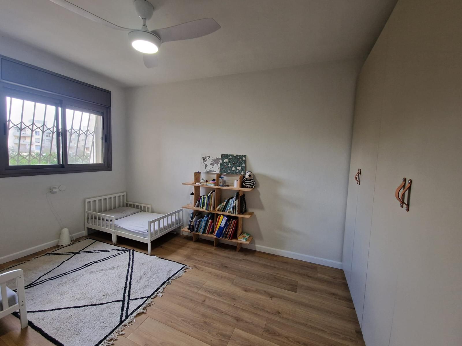 חדר שינה עם שתי מיטות, מדף ספרים ומאוורר תקרה.