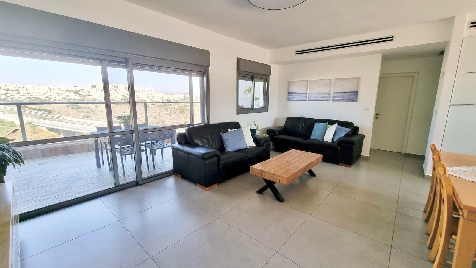 סלון עם ספה, שולחן, כיסאות ומרפסת.