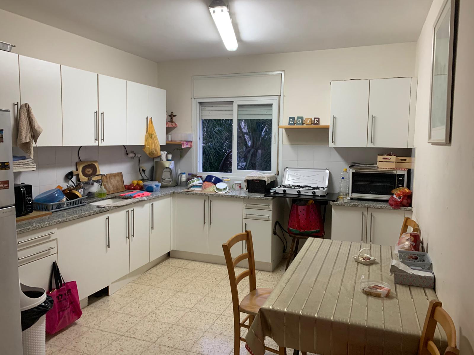 מטבח עם ארונות לבנים, שולחן וכיסאות.