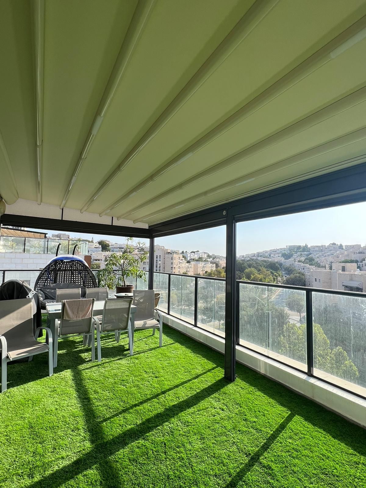 מרפסת עם פרגולה ועליה שולחן וכיסאות.