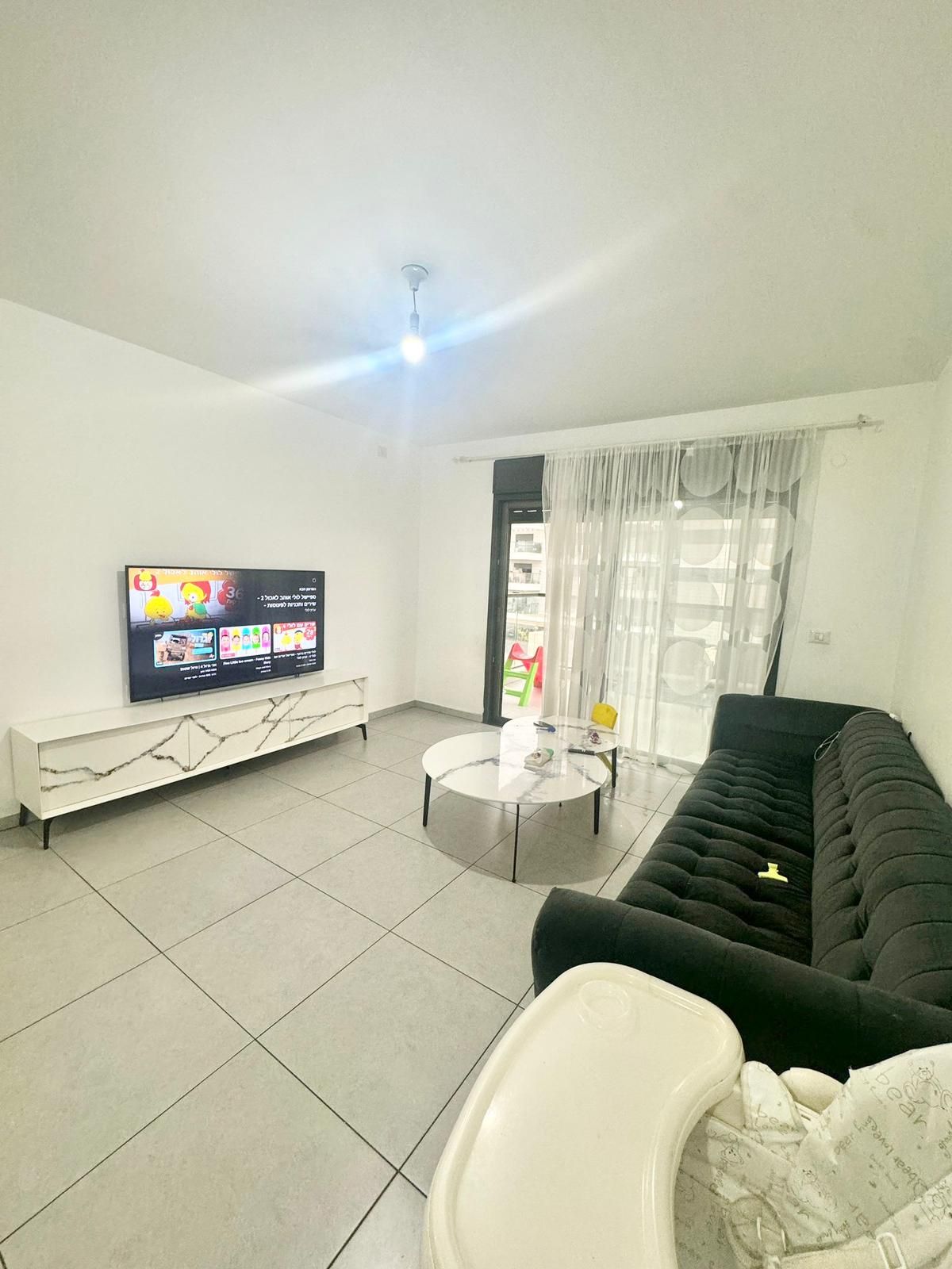 סלון עם ספה שחורה וטלוויזיה בעלת מסך שטוח.