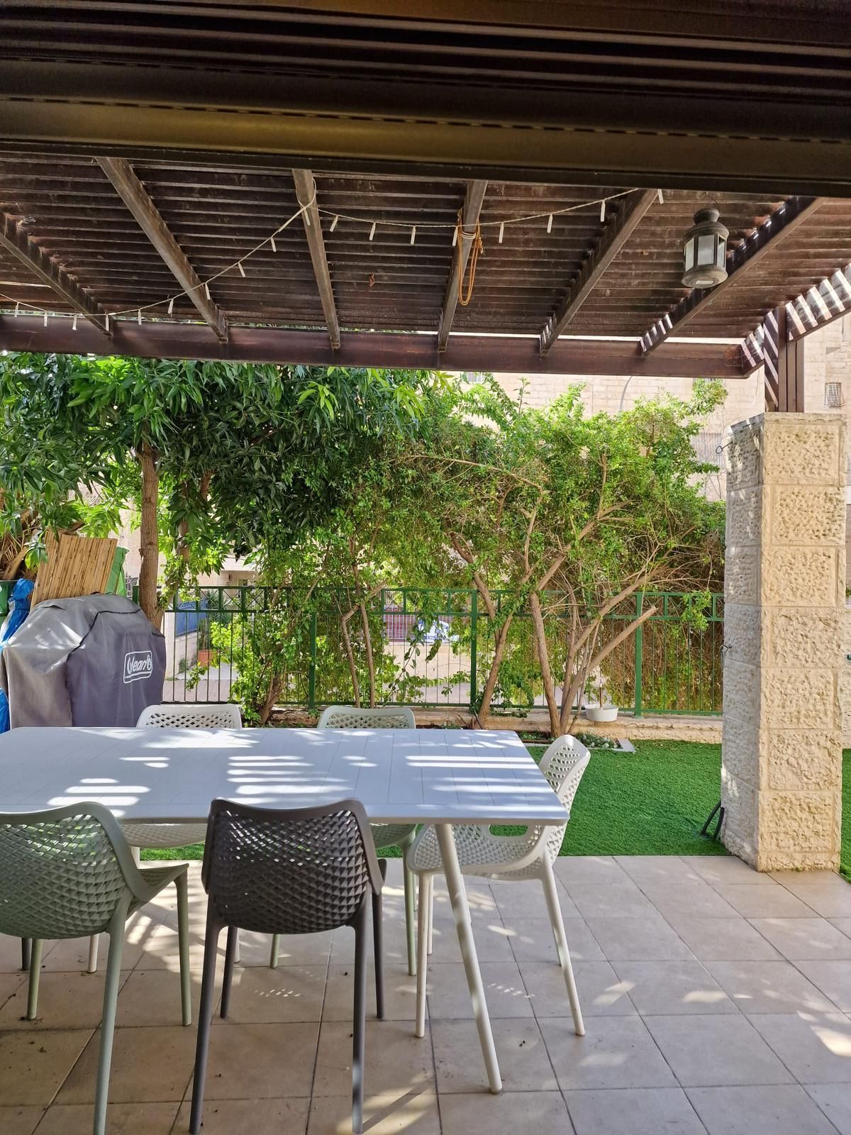 פטיו עם שולחן וכיסאות מתחת לפרגולה.