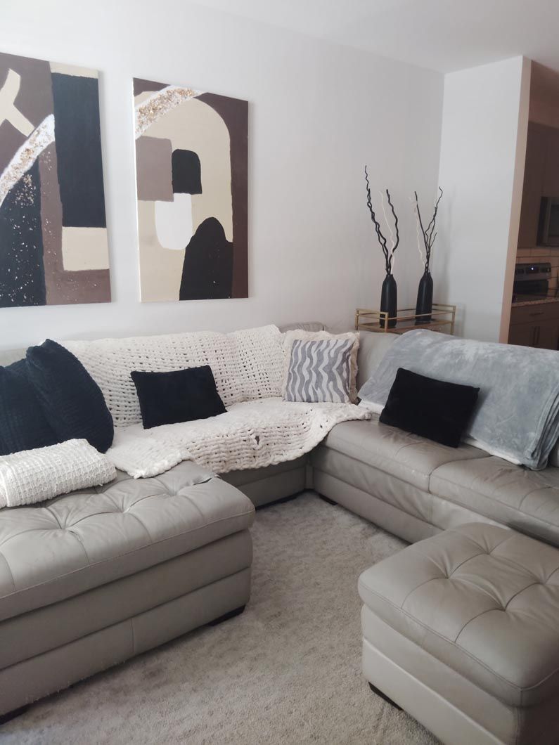 A beige sectional sofa in a living room with black pillows, a white throw blanket, and two abstract wall paintings.