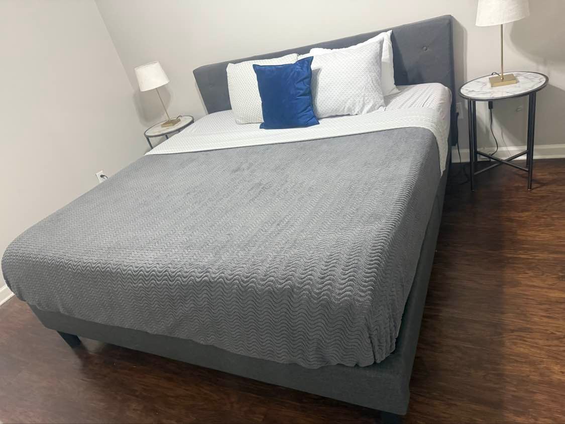 A bed with grey bedding, pillows, and side tables with lamps in a room with wooden floors.