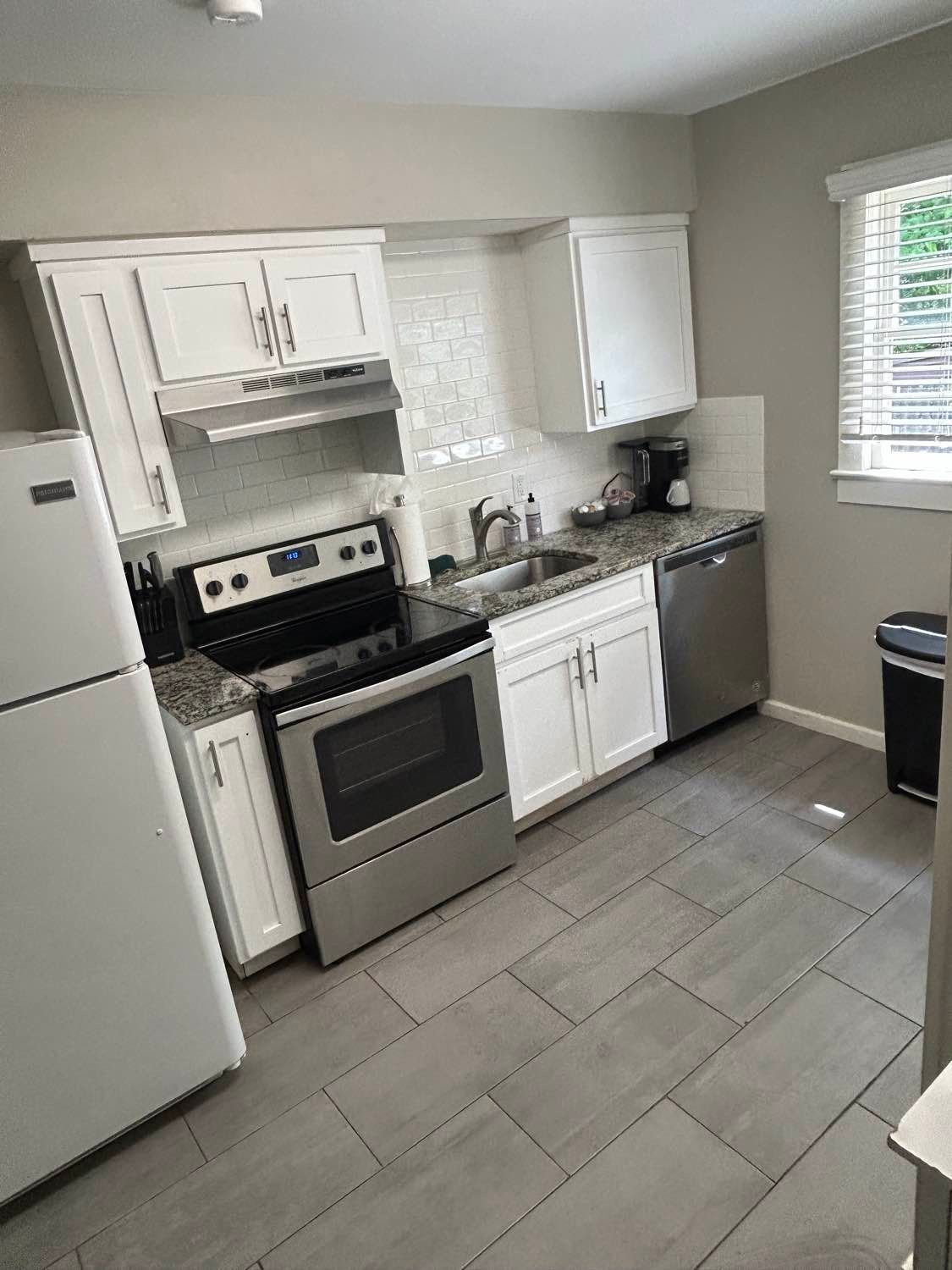 White kitchen with stainless steel appliances, white cabinets, and gray tiled floor.