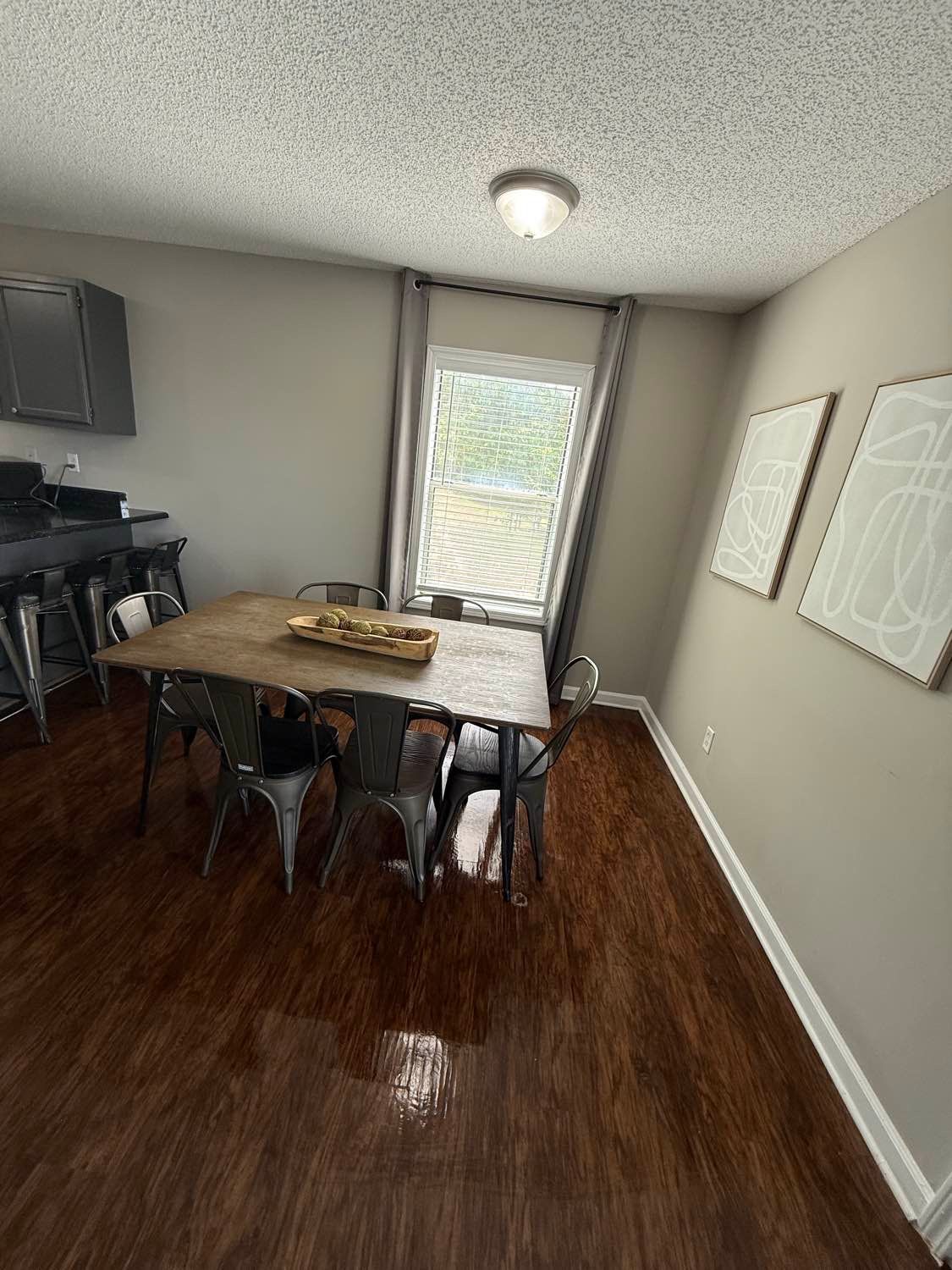 Dining room with a wooden table, metal chairs, and modern artwork. Dark wood floors and gray walls.