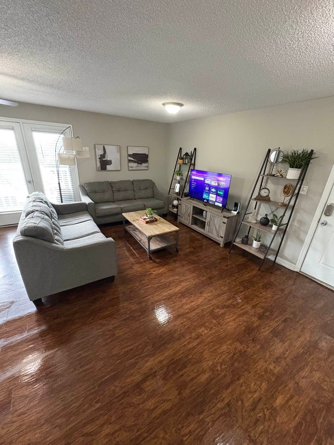 Living room with gray sofas, wood floor, TV, coffee table, and shelves.
