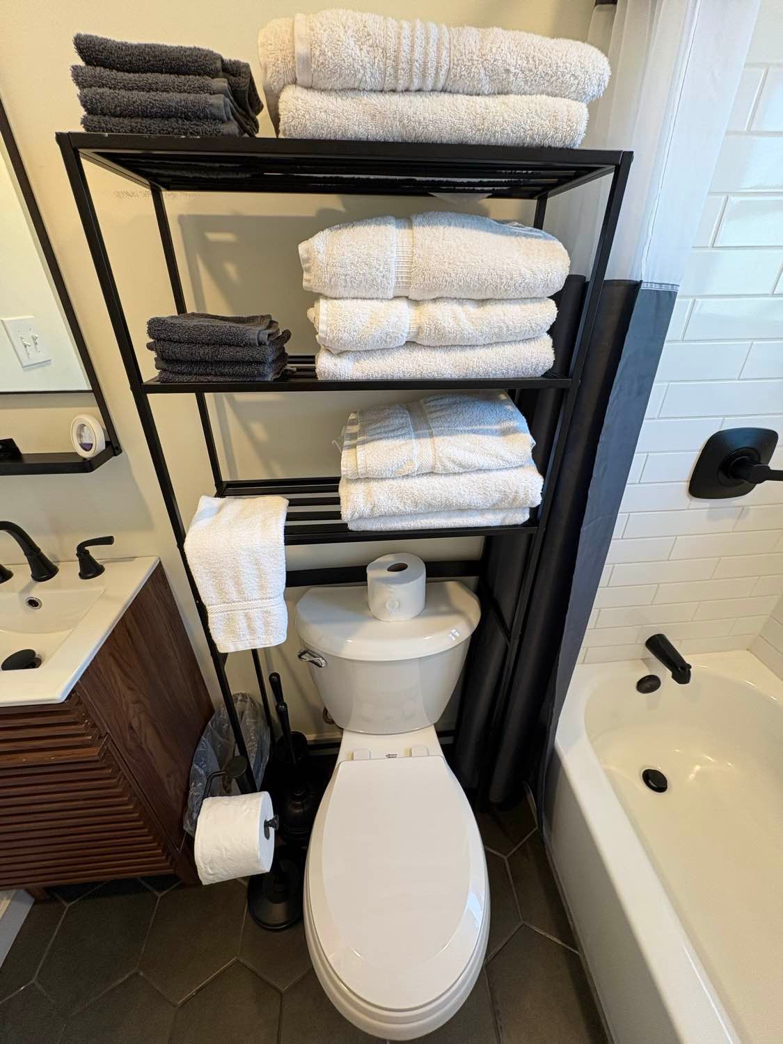 Bathroom with black shelving holding white and gray towels over a toilet.