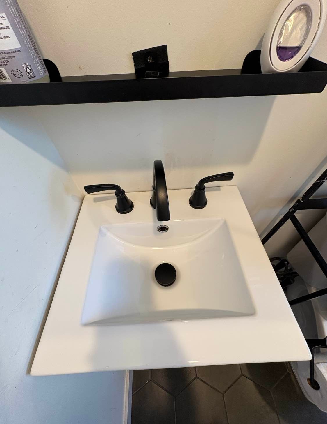 Bathroom sink with black faucet and fixtures, white countertop, and a black shelf above.