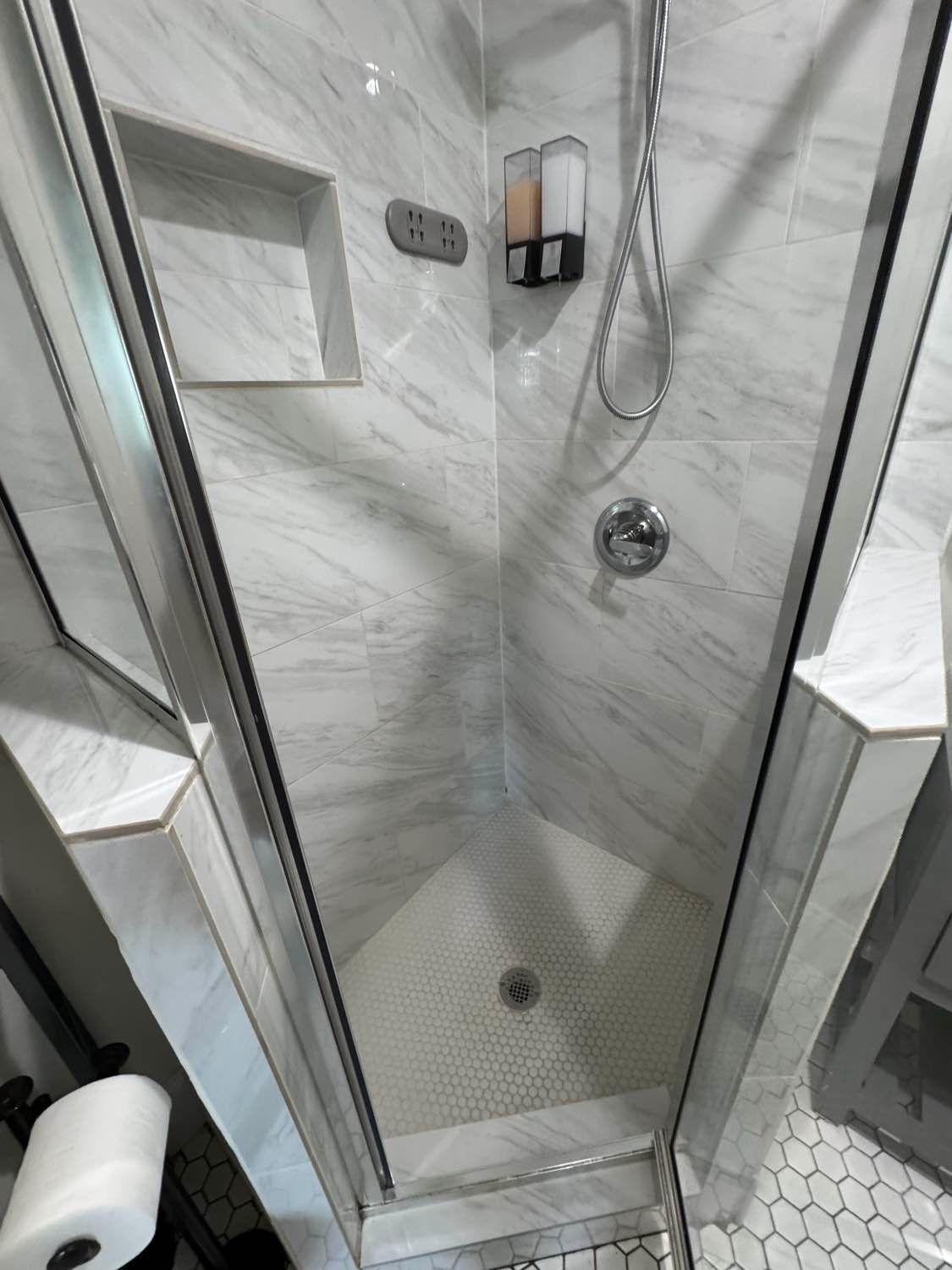 Shower stall with glass doors, marble-like tile, built-in shelf, and chrome fixtures.