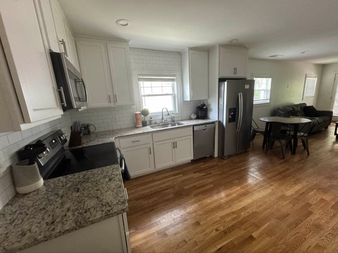 Bright kitchen with white cabinets, granite countertops, stainless steel appliances, and hardwood floors.