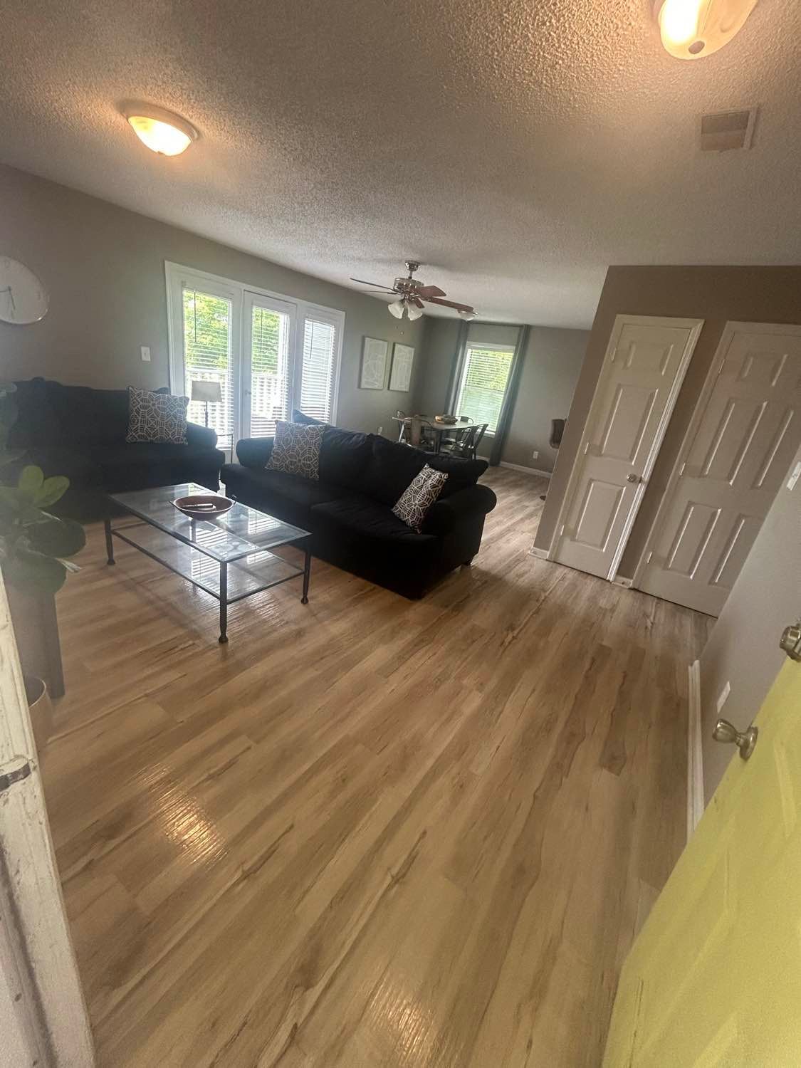 Living room with black sofas, glass coffee table, and wood floors. French doors lead outside.