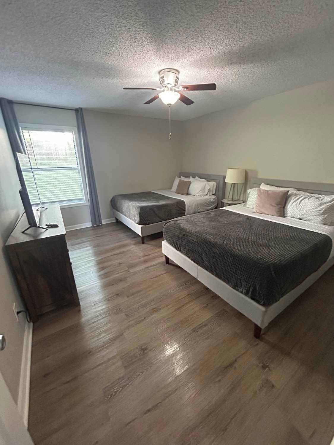 Bedroom with two beds, wood floor, and a window with blue curtains.