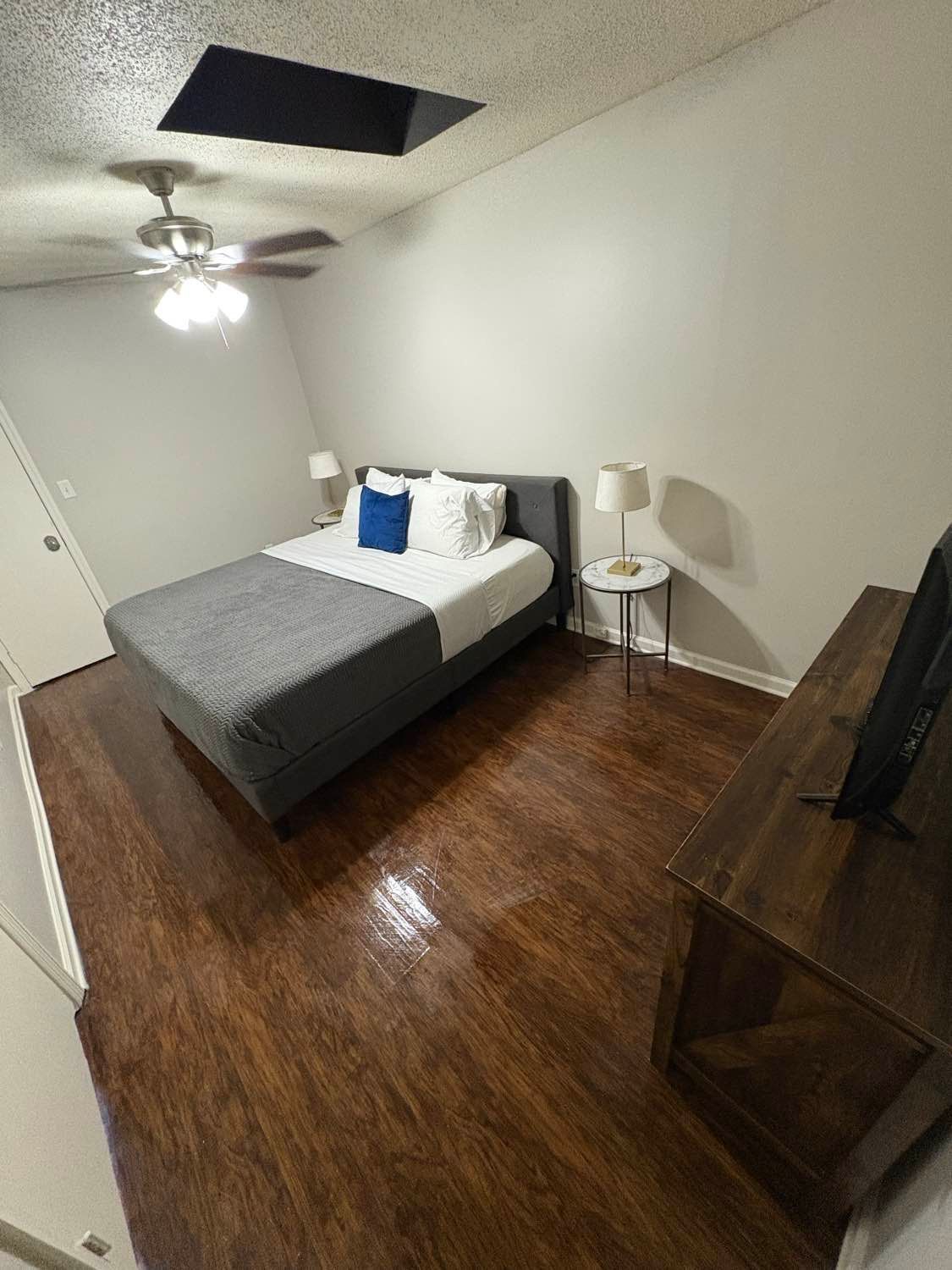 Bedroom with gray bed, wooden dresser, brown floor, and ceiling fan.