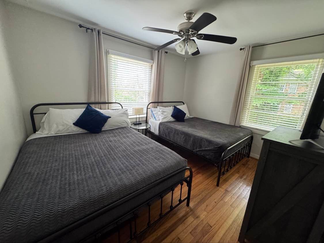 Bedroom with two twin beds, grey bedding, window, wood floors, and dark dresser.
