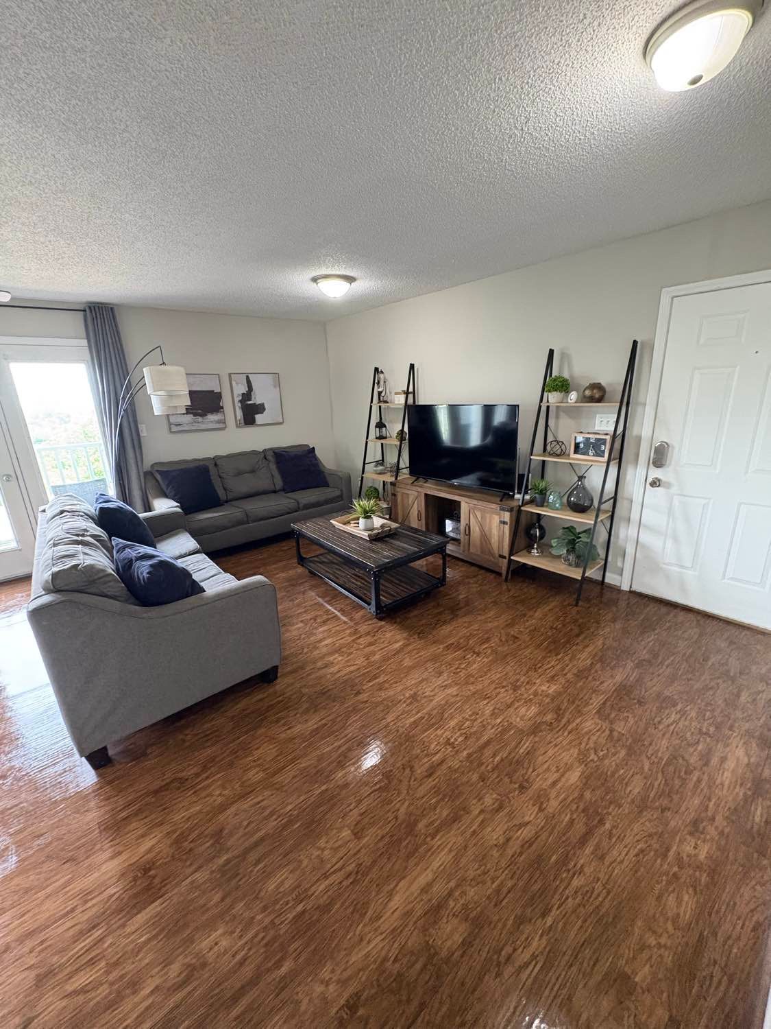 Living room with gray couches, wooden floors, a TV, and shelves; neutral tones.