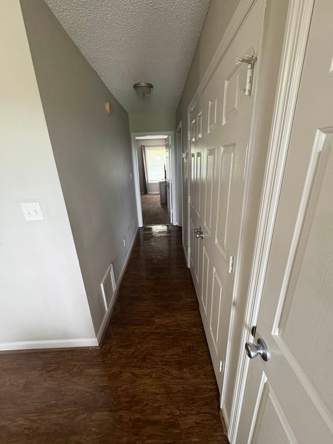 Narrow hallway with brown floor, white doors, gray wall, and light at the end.