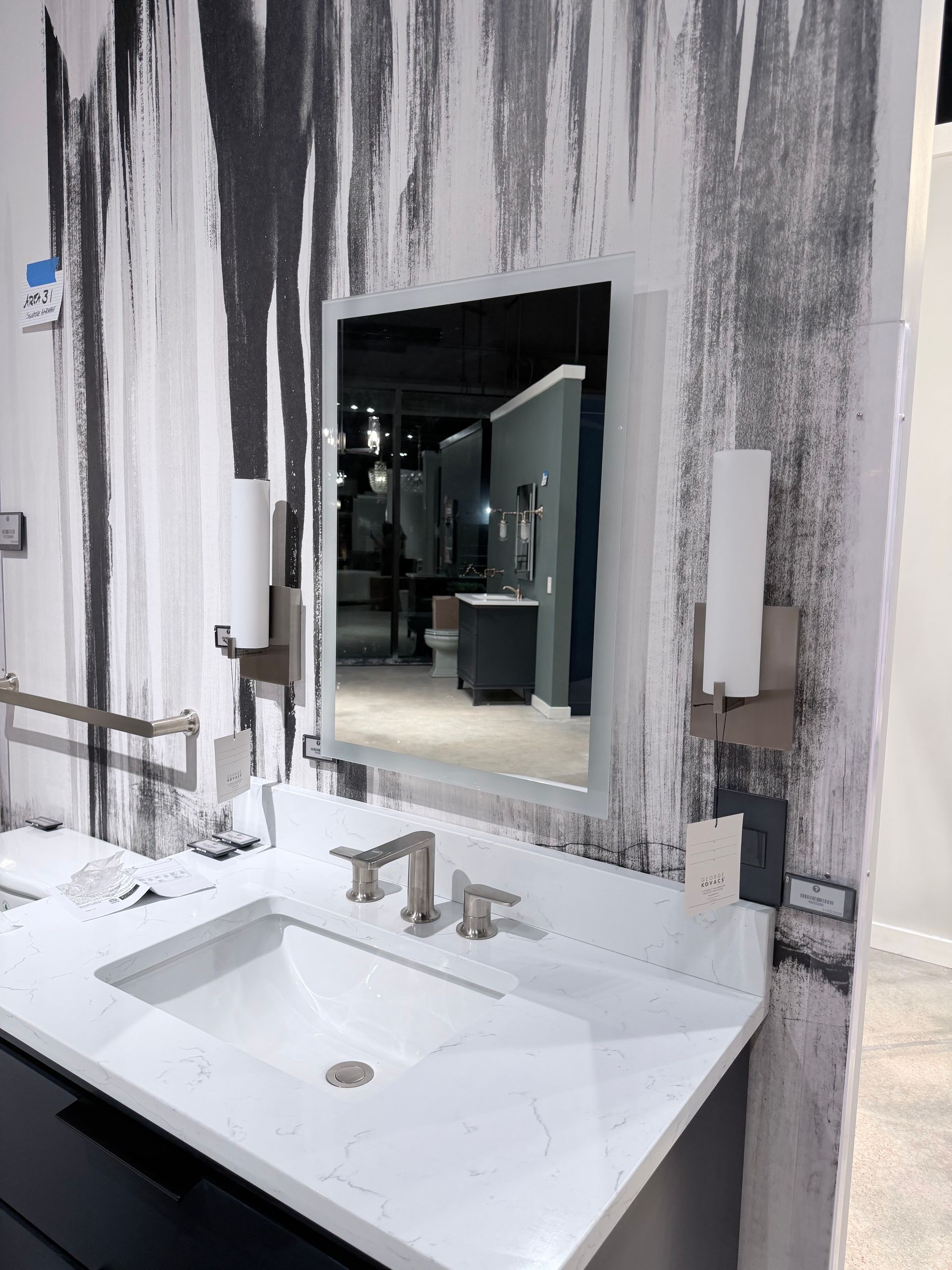 A modern bathroom vanity with a white quartz countertop, black cabinets, and a mirror against a black and white wall.