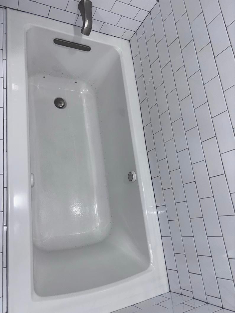 An overhead view of a white bathtub set against white subway tile walls.