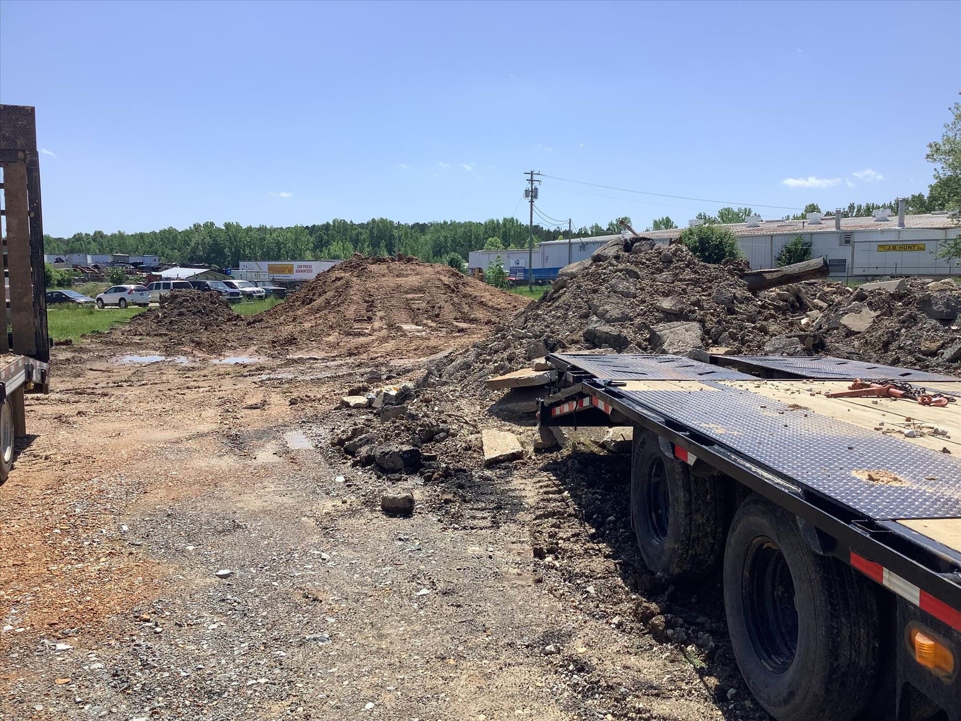 A flatbed truck is parked in a dirt lot next to a pile of dirt.