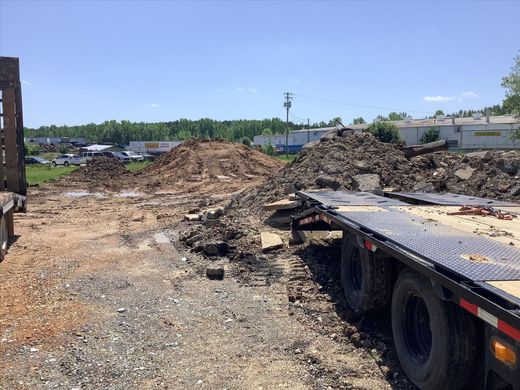 A flatbed truck is parked in a dirt lot next to a pile of dirt.