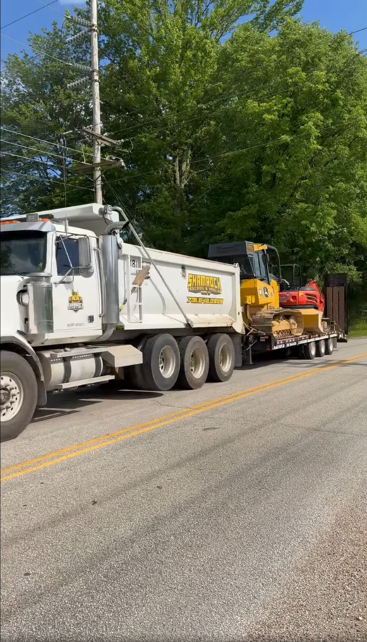 A dump truck is parked on the side of the road next to a bulldozer.