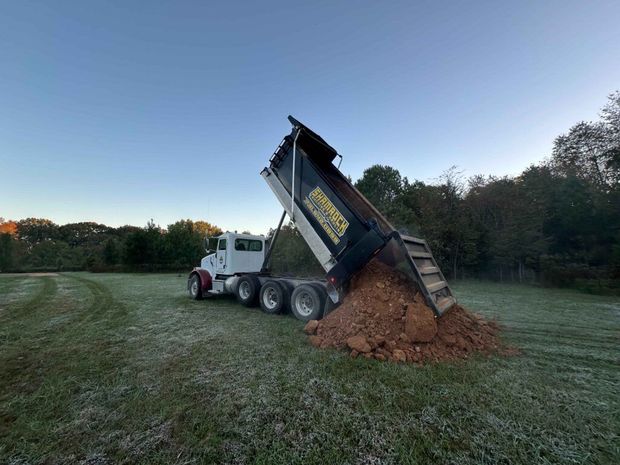 A dump truck is dumping dirt into a field.