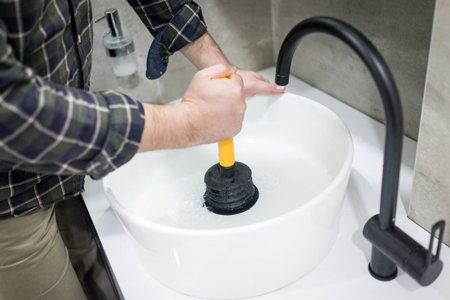 Plumber's hand using plunger in bathroom sink